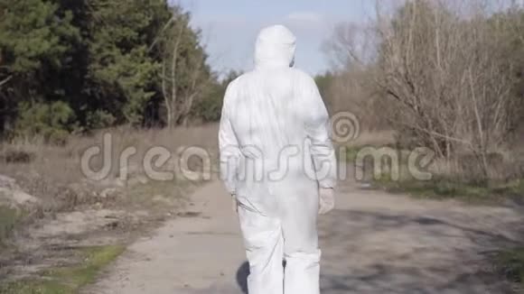 公园里穿着白色安全服和面罩走在小巷里的男性病毒学家的后景男人在户外散步视频的预览图