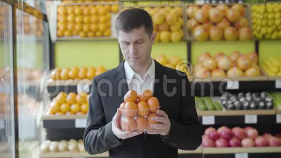 快乐的男性杂货店顾客闻着新鲜美味的橘子对着镜头微笑的肖像成年白种人视频的预览图