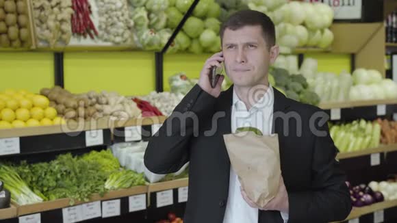一张深色棕色眼睛的白人男子在杂货店打电话的画像有自信的成年人拿着背包视频的预览图