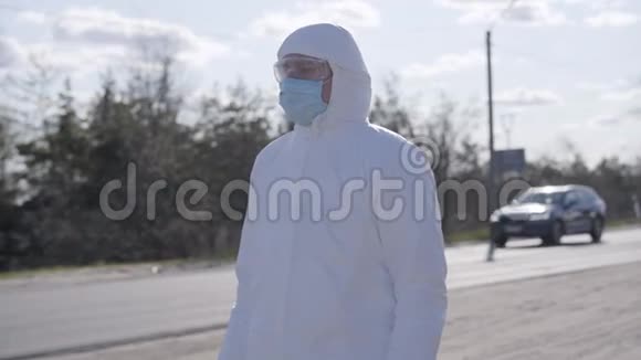 严肃的年轻人穿着白色的安全防护服站在郊区的路上戴面罩的高加索病毒学家视频的预览图