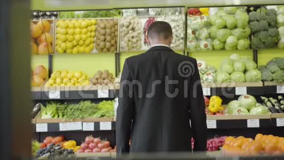 穿着西装的白种人年轻男子从货架上看着杂货店里的水果和蔬菜视频的预览图