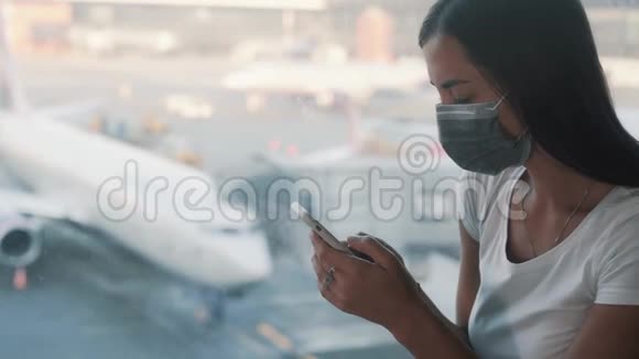 戴防护面罩的女士使用智能手机在机场发送信息视频的预览图