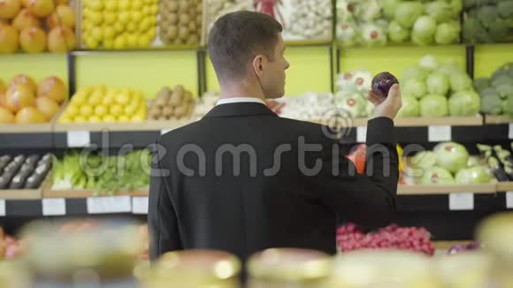 在杂货店里闻到红洋葱味的黑种人年轻人的后景穿西装的成年男子的后视图视频的预览图