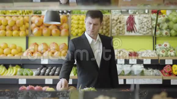 穿西装的白种人在杂货店选择猕猴桃自信的成年商人购买浆果的肖像视频的预览图