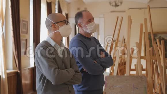 两个戴着医疗面具的人站在画廊里看展览视频的预览图