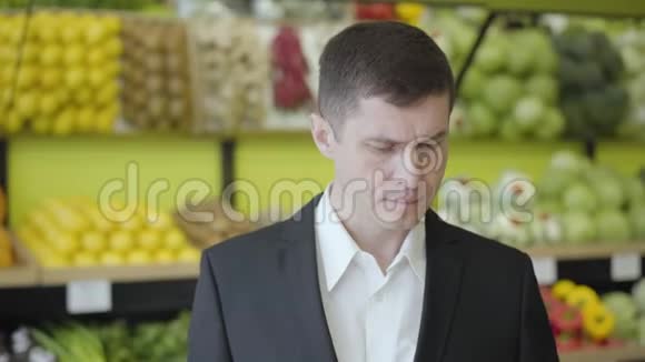 严肃的高加索男人在杂货店里选择梨的特写帅哥闻着黄色水果视频的预览图