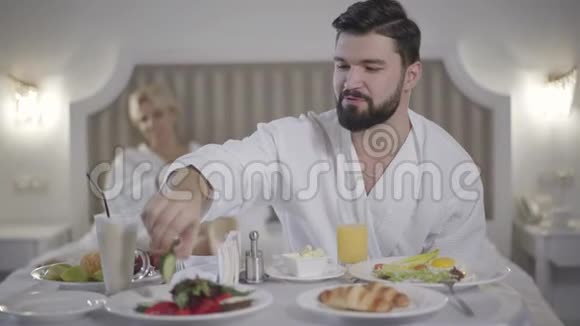 阳性白种人男子吃黄瓜的肖像模糊的妇女躺在背景与药片快乐快乐视频的预览图