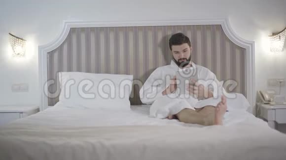 年轻英俊的白种人晚上躺在床上用平板电脑的肖像喜欢留胡子的人在社交网站上视频的预览图