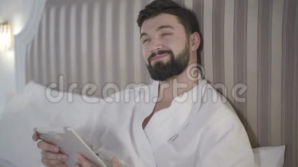 用平板电脑和微笑特写高加索人的肖像社交媒体上的帅哥胡子短信视频的预览图