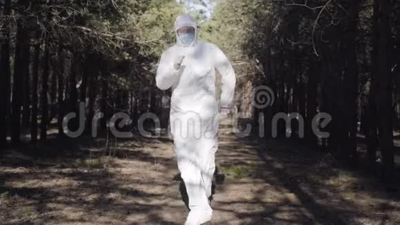 穿着白色防护服眼镜和面罩的年轻白种人的滑稽舞蹈活跃的男人在森林里跳舞视频的预览图