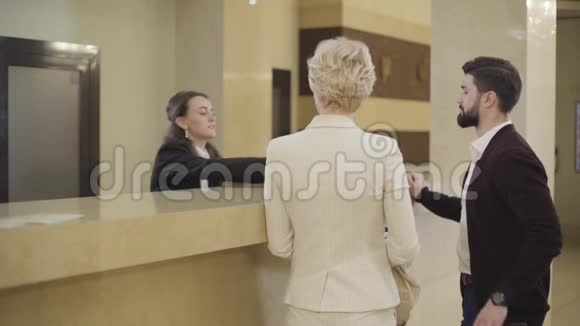 年轻的高加索女性接待员给男人签名房间钥匙卡给女人富有的夫妇视频的预览图