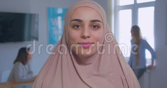 一个年轻美丽的微笑自信的穆斯林女孩在头巾办公室背景的特写肖像视频的预览图