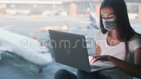 戴防护医疗面罩的妇女使用笔记本电脑在机场工作视频的预览图