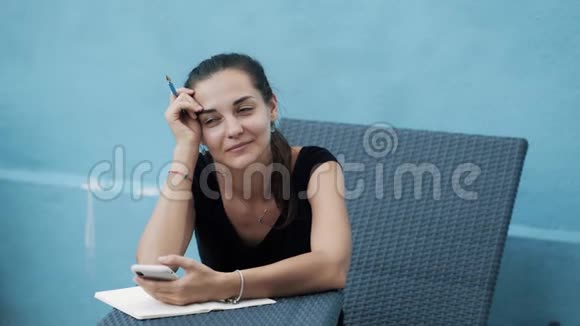 年轻女子坐在日光浴床上写日记使用移动蓝色背景视频的预览图