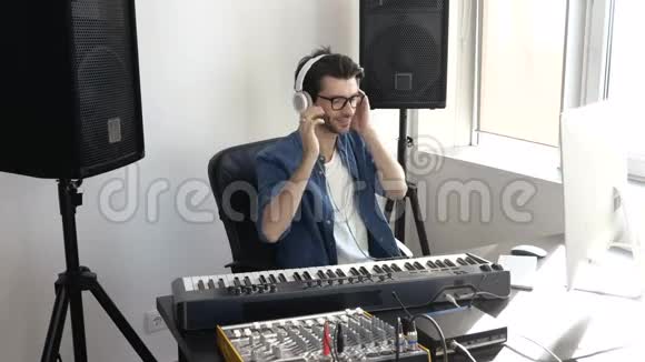 录音室的年轻人他坐在桌子旁用音乐混合控制台和电脑录音音乐视频的预览图