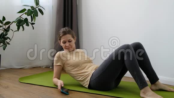 在家做运动的中年妇女在房间里用移动应用进行女性健身训练视频的预览图