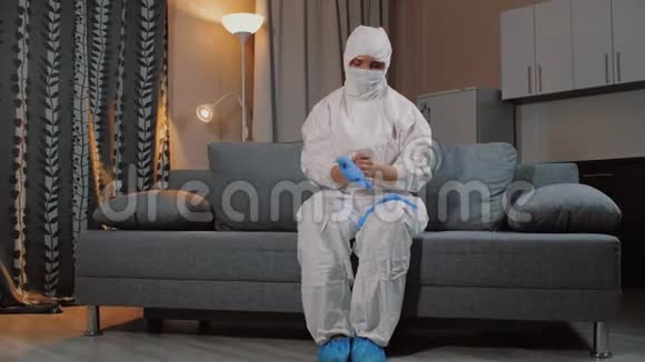 男人穿着防护服坐在家里的沙发上戴上手套视频的预览图