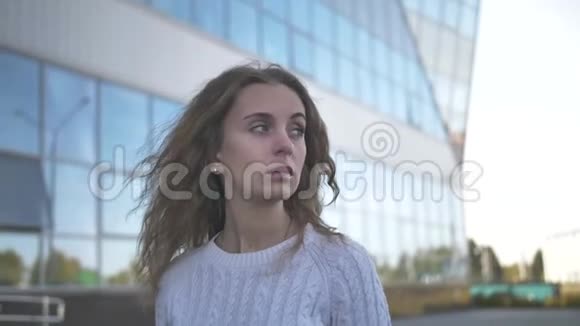 一个穿着白色毛衣神情悲伤的女孩站在一栋商业大楼的背景上视频的预览图