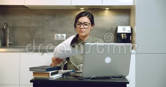专注于戴眼镜的年轻女性在笔记本电脑上工作在家阅读财务报告或合同远程工作视频的预览图
