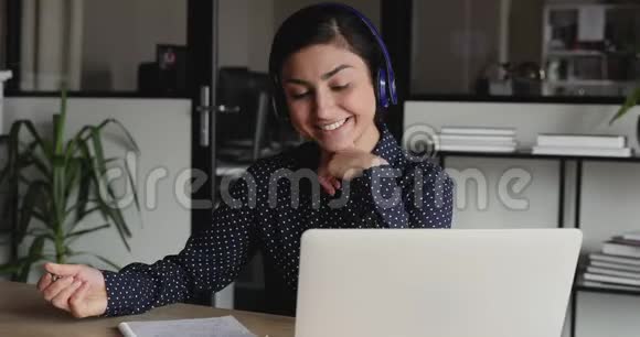 戴着耳机看着笔记本电脑做笔记的印度女孩微笑视频的预览图