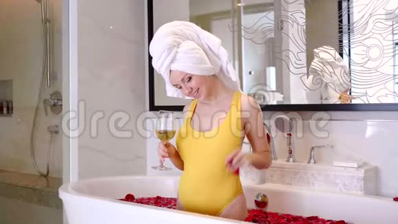 幸福的微笑年轻女子拿着玫瑰花瓣洗澡拿着香槟杯视频的预览图