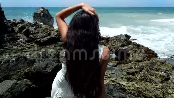 拉丁女孩坐在靠近大海的岩石海岸上视频的预览图