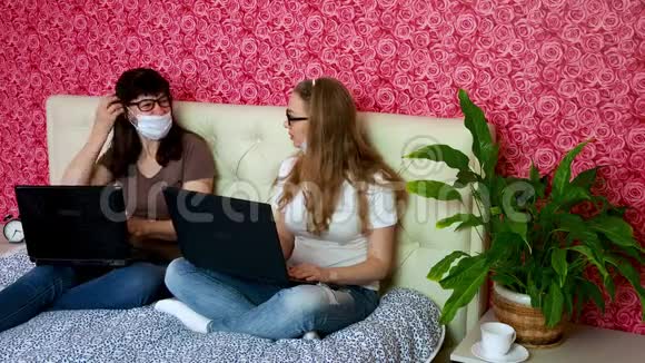 从家里远程工作两名戴着医用防护面罩的白人妇女正在卧室的笔记本电脑上工作视频的预览图