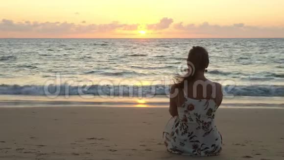 日落时分穿着时尚服装的年轻女子坐在海滩上视频的预览图