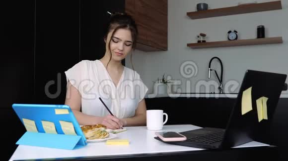 检疫期间厨房里的年轻女子坐在桌边学习或学习使用平板电脑笔记本电脑和远程工作视频的预览图