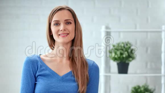随意的女人微笑着摆着白色房间内部的肖像中型近距离拍摄4k红色相机视频的预览图