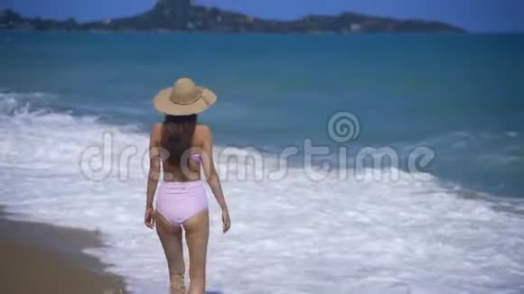 一个戴草帽的漂亮女孩沿着海滩散步巨大的海浪在海滩上翻滚视频的预览图