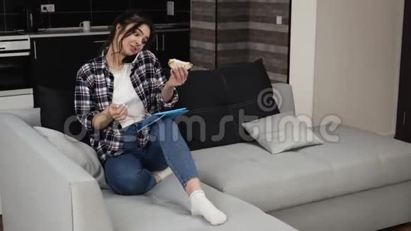 检疫期间厨房里的年轻女子坐在沙发上用平板电脑上网打电话吃饭视频的预览图