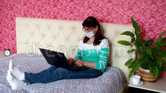 从家里远程工作一名白人成年妇女正在卧室里的笔记本电脑上工作床上有一张保护性医疗设备视频的预览图