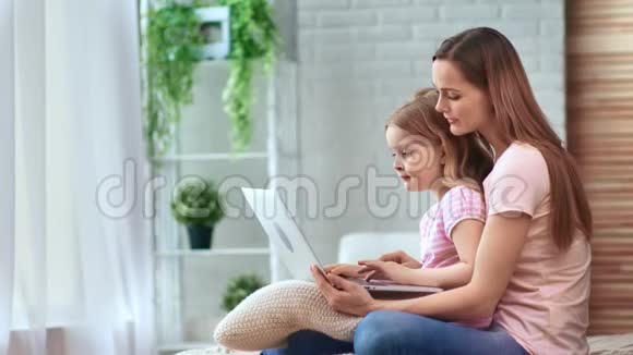 积极的金发女性和漂亮的孩子使用电脑坐在床上中型摄影机视频的预览图