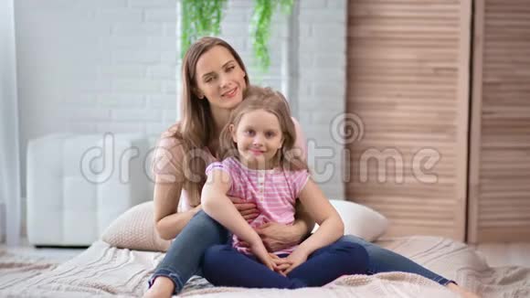 嬉笑的女人抱着无忧无虑的小女孩坐在床上4k龙红相机视频的预览图