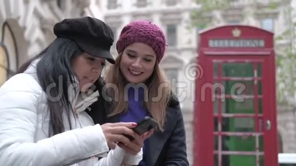 两个女孩用红色的电话亭看着伦敦大街上的手机视频的预览图