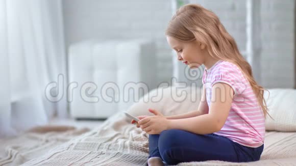 可爱的小女孩在舒适的家里放松使用平板电脑坐在床上4K红色相机拍摄视频的预览图