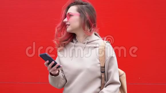 时尚肖像美丽的微笑时髦女人戴太阳镜红色头发与智能手机对抗视频的预览图