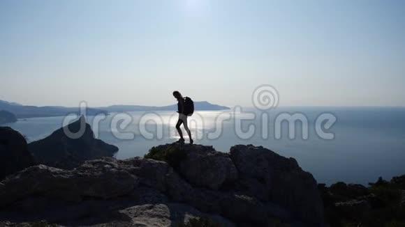 运动建筑的年轻女孩爬上了一个高高的悬崖看着美丽的阳光与大海A视频的预览图