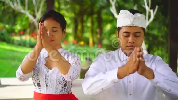 巴厘岛的印度教家庭在寺庙里祈祷巴厘夫妇的前额有双手视频的预览图