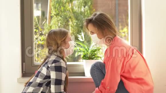 年轻的女人和一个带着医用口罩的学龄女孩正在窗口边聊天检疫视频的预览图