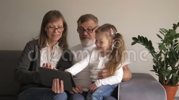 孩子和祖父母使用PC平板电脑可爱的中年夫妇和他们的小孙女用数码平板电脑视频的预览图