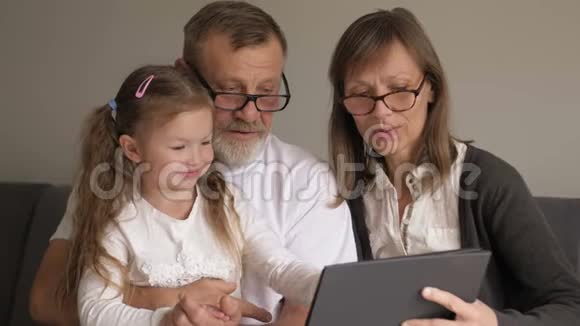 小女孩和祖父母坐在一起玩平板电脑孩子玩高级男女快乐视频的预览图