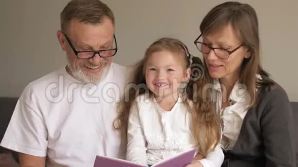 可爱的祖父母和他们的孙子坐在书上一起读有趣的故事的画像视频的预览图