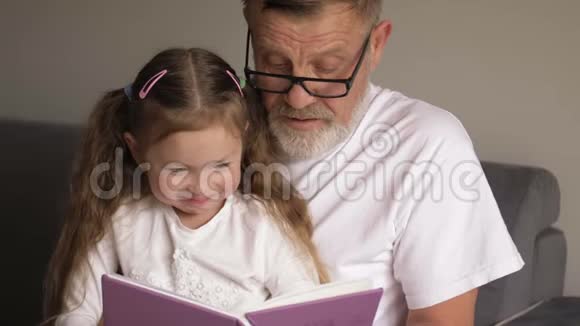 祖父戴眼镜的肖像画和可爱的小孙女坐在一起看书视频的预览图