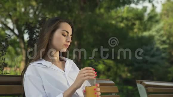 美丽的女人在公园里喝橙汁放松视频的预览图