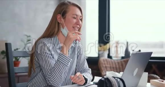 年轻健康快乐的医生女人在笔记本电脑上打视频电话到家里工作在线咨询人们戴着口罩视频的预览图