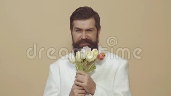 大胡子拿着花束时尚帅哥在看镜头的肖像穿着优雅白色的英俊男人视频的预览图