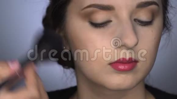 为坐在工作室的美丽而华丽的女人化妆化妆师使用粉末视频的预览图