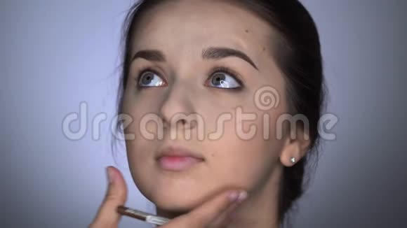 为坐在工作室的美丽而华丽的女人化妆的过程化妆师画眼线视频的预览图